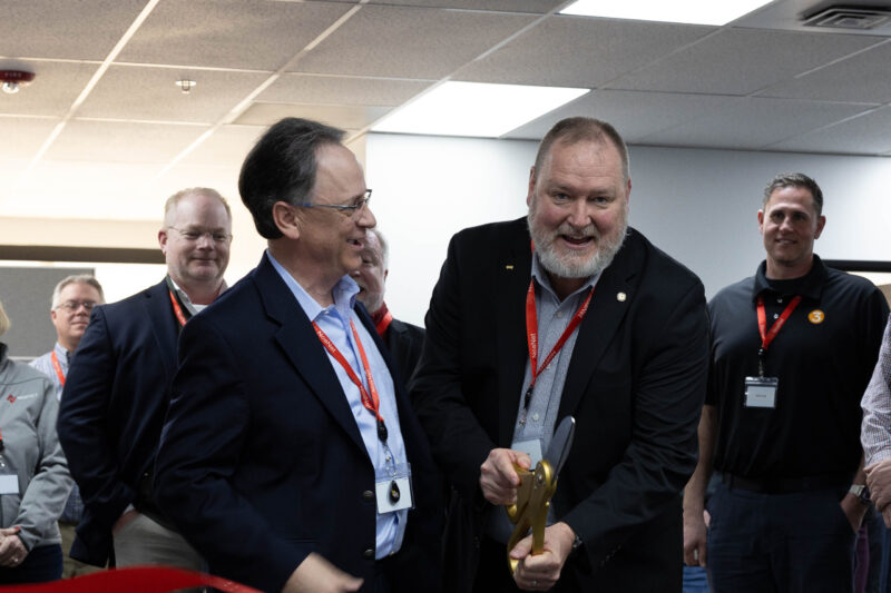 Craig Nelsen, NoaNet CEO, and Adam Wasserman, State 911 Coordinator, who is wielding a pair of over-sized golden scissors for the ceremonial ribbon cutting.